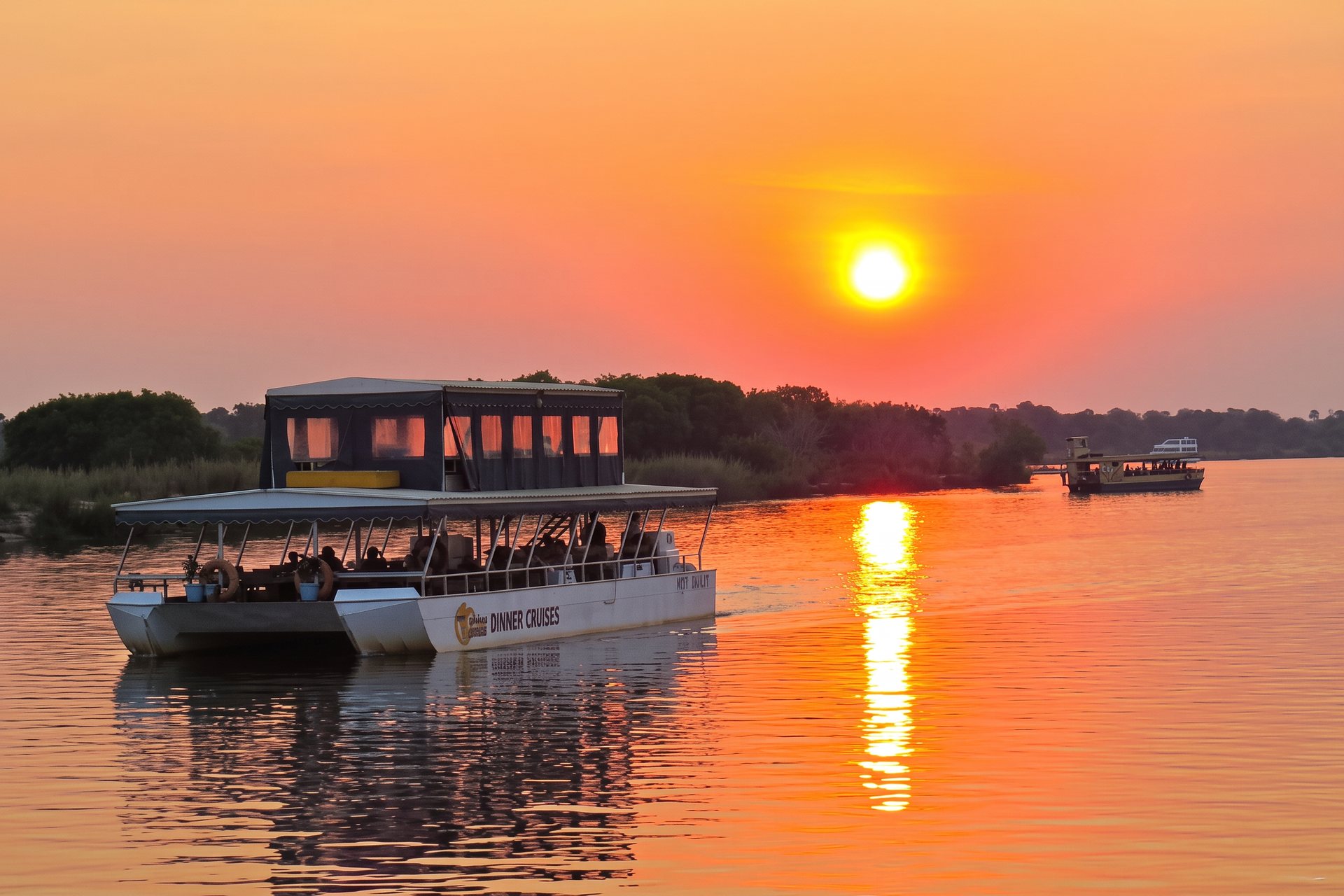 A river cruise boat drifting along the Zambezi as the sun sets